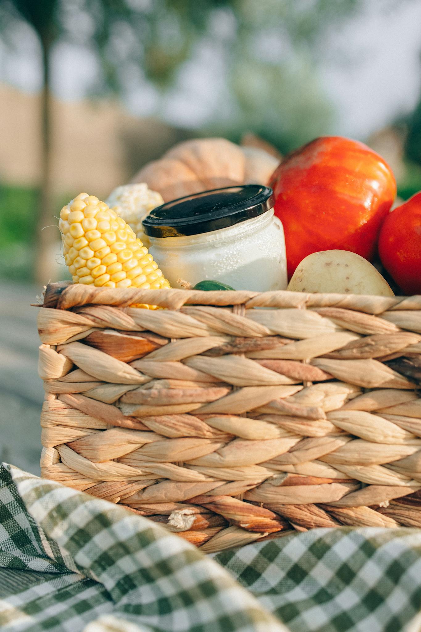 A close-up of fresh organic vegetables and jar in a woven basket outdoors.