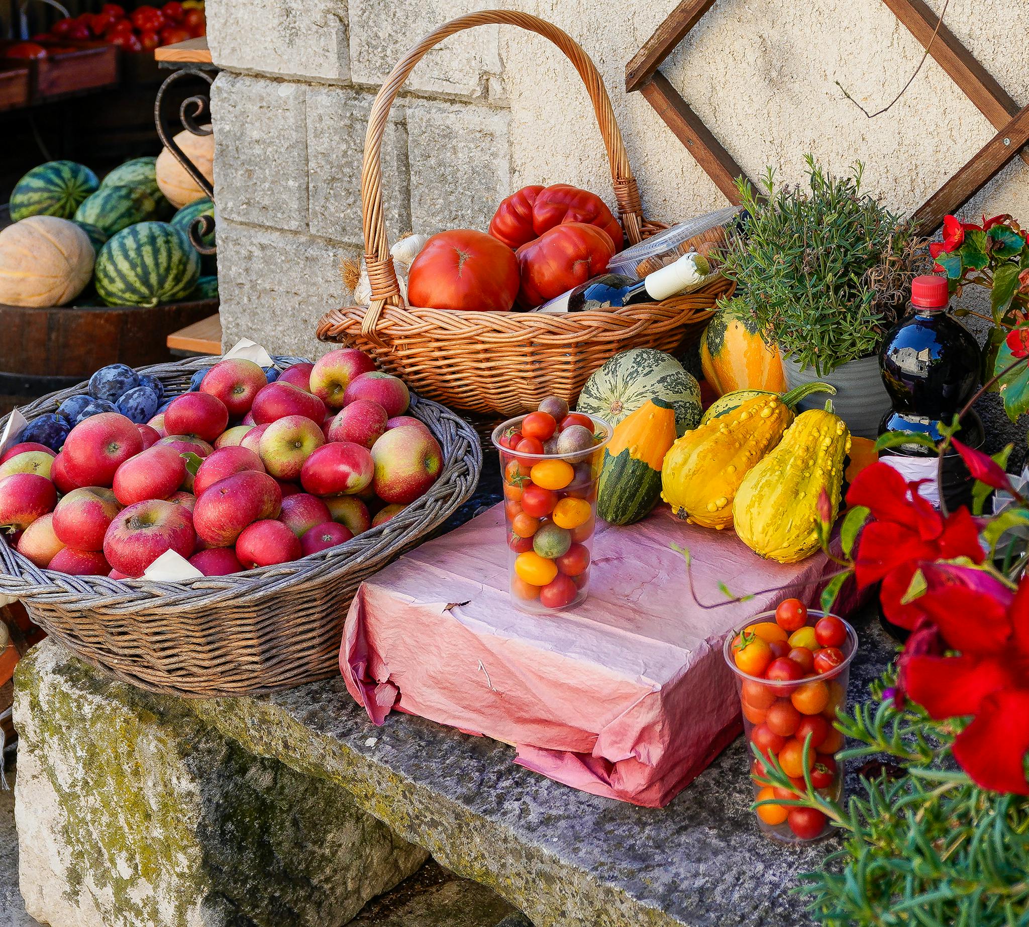 A variety of fresh fruits and vegetables displayed at an outdoor farmer's market. Vibrant, local produce including apples, tomatoes, squashes, and herbs.